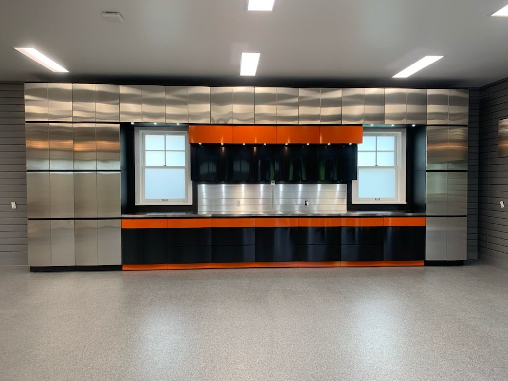 Garage avec armoires en acier inoxydable, touches orange et noires et deux fenêtres.
