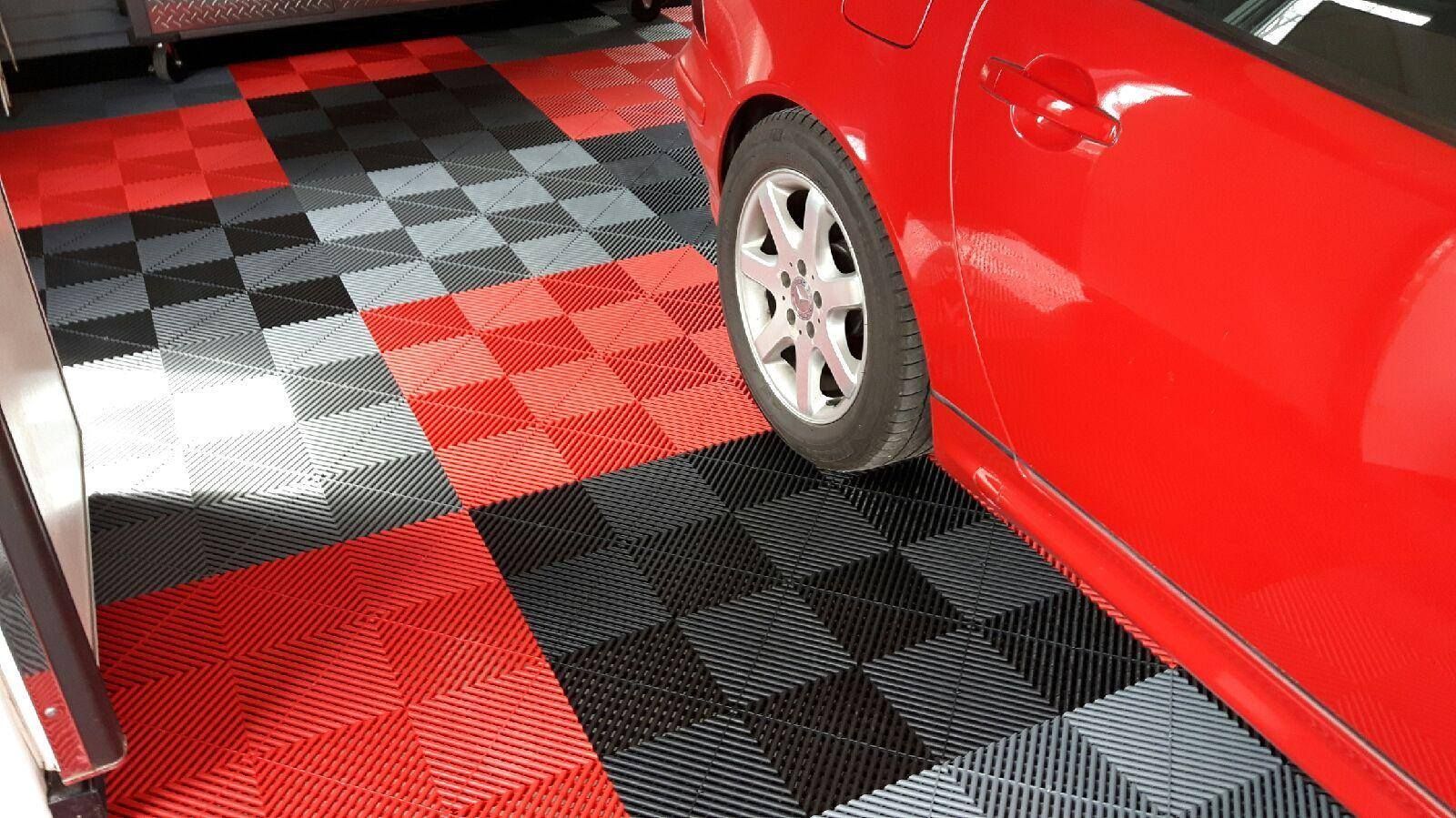 Voiture rouge garée dans un garage dont le sol est carrelé de carreaux à damier rouges, noirs et gris.