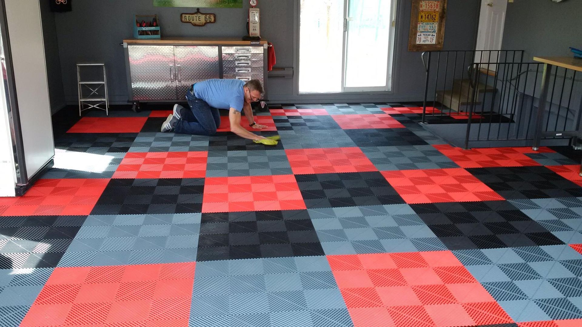 Un homme installe des dalles de sol emboîtables rouges, noires et grises dans un garage.