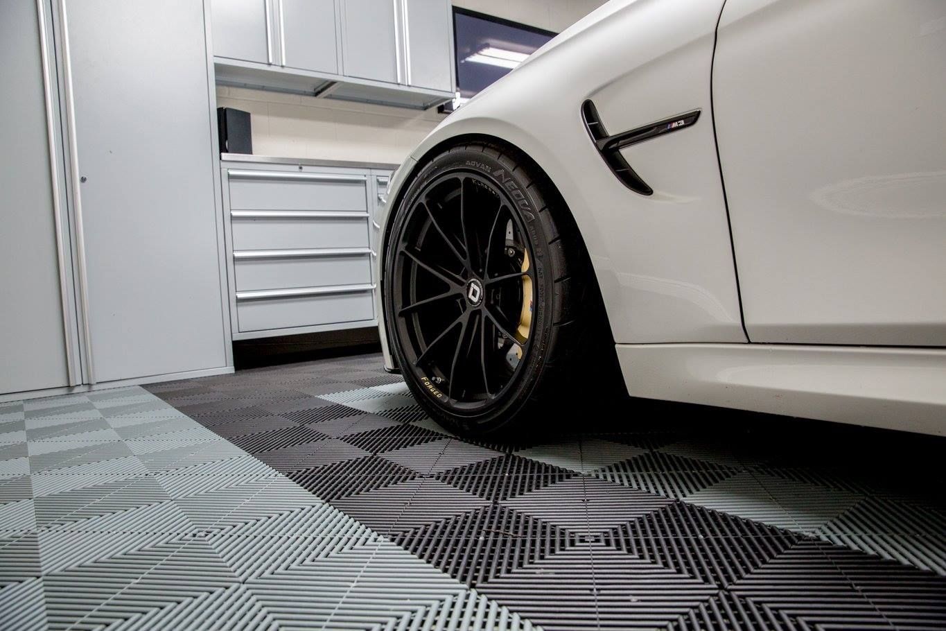 Roue de voiture blanche sur un sol de garage carrelé noir et gris, placards en arrière-plan.