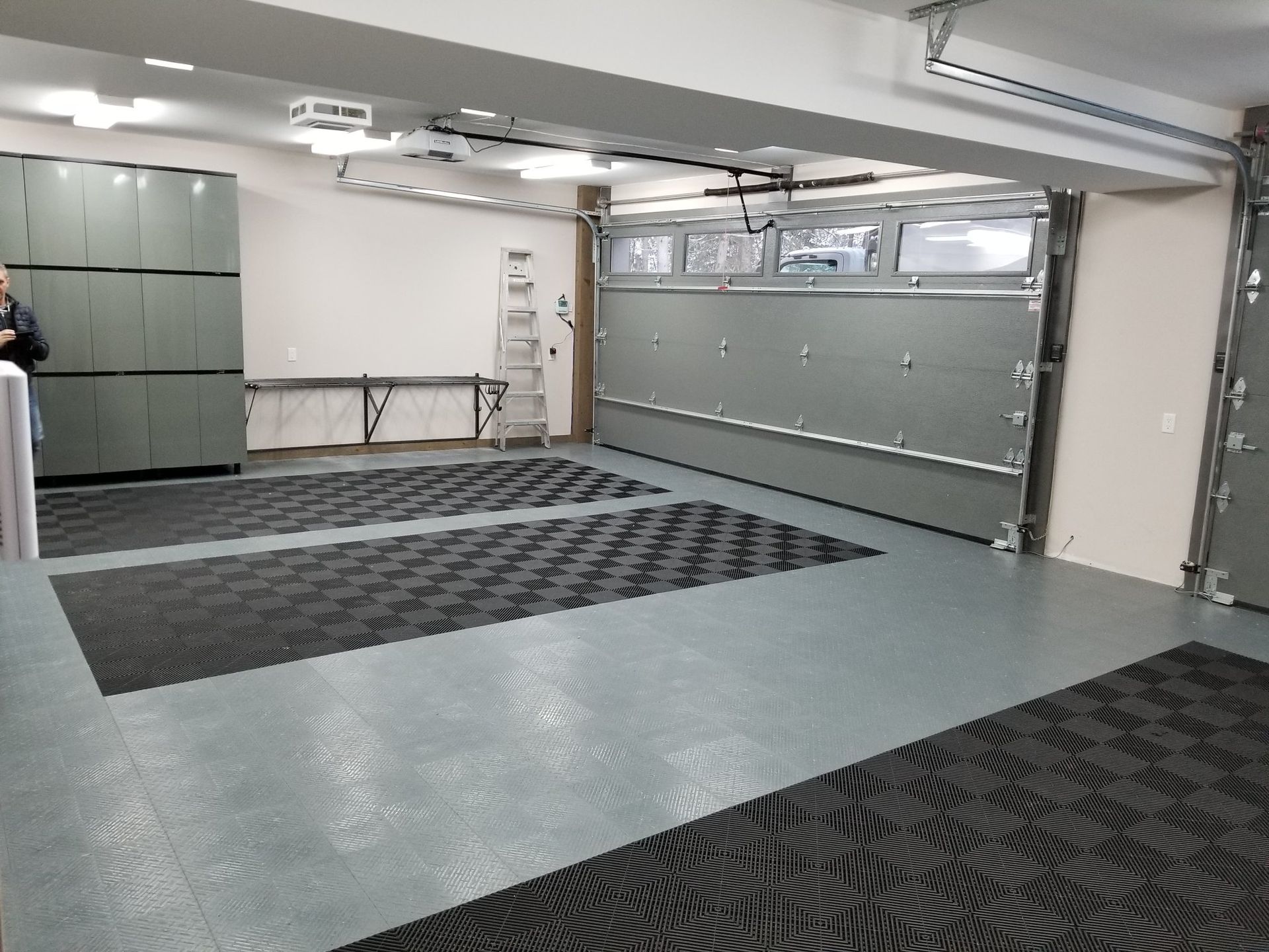 Garage spacieux et bien éclairé avec porte ouverte, placards de rangement et tapis de sol texturés.