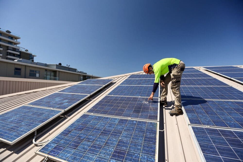 A Man Is Installing Solar Panels On The Roof Of A Building — Solarblu Pty Ltd In Wollongong, NSW