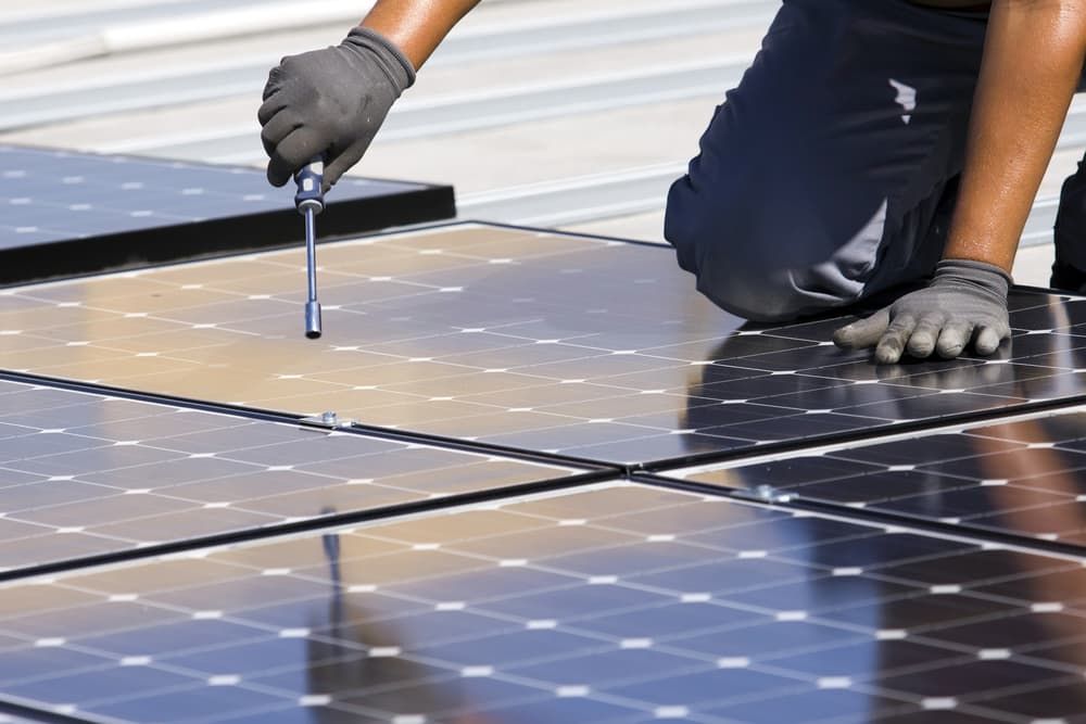 A Man Is Installing Solar Panels On A Roof — Solarblu Pty Ltd In Moss Vale, NSW