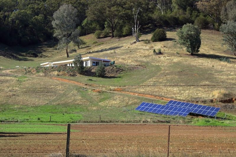 A Row Of Solar Panels Are Sitting In A Field Next To A House — Solarblu Pty Ltd In Tullimbar, NSW