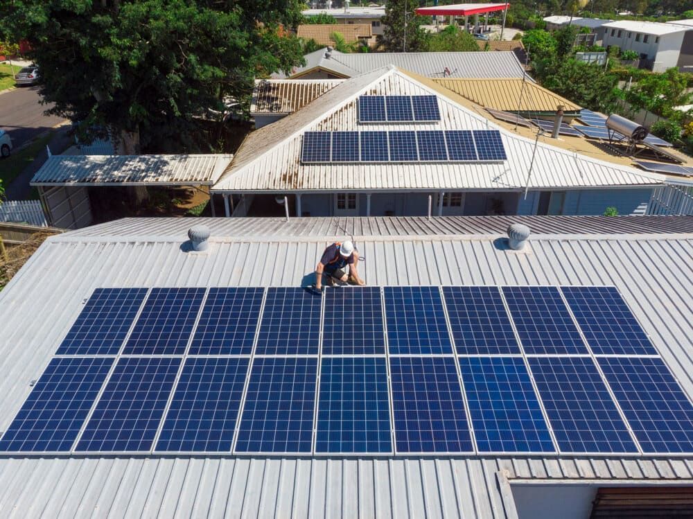A Man Is Installing Solar Panels On The Roof Of A House — Solarblu Pty Ltd In Woonona, NSW