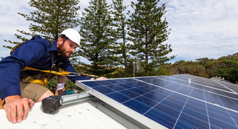 A Man Is Installing Solar Panels On A Roof — Solarblu Pty Ltd in Kangaroo Valley, NSW