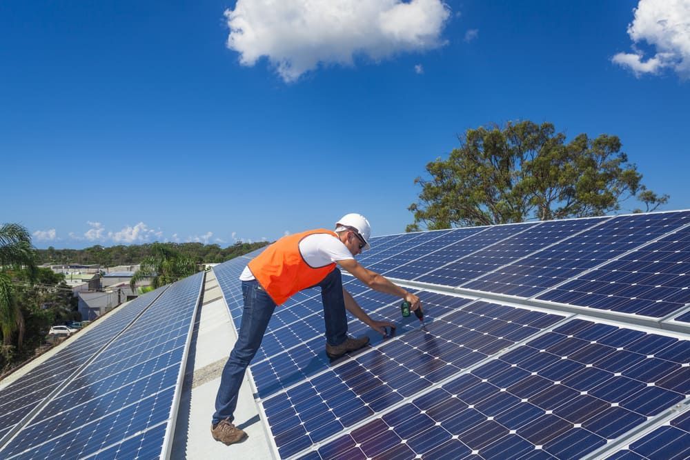A Man Is Installing Solar Panels On The Roof Of A Building — Solarblu Pty Ltd In Calderwood, NSW