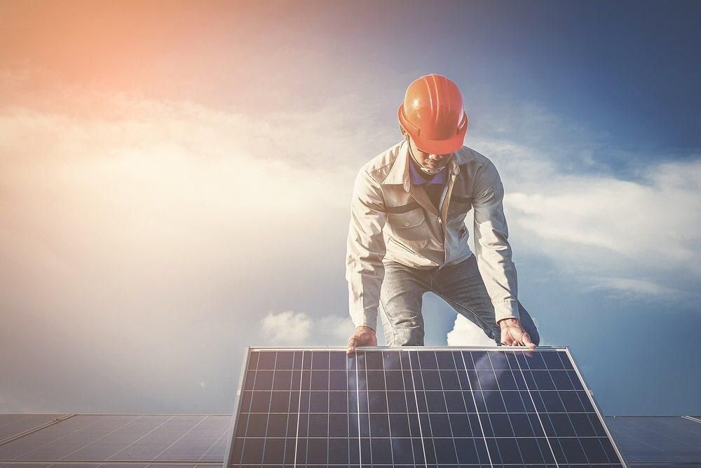 A Man Wearing A Hard Hat Is Kneeling On Top Of A Solar Panel — Solarblu Pty Ltd In Tullimbar, NSW