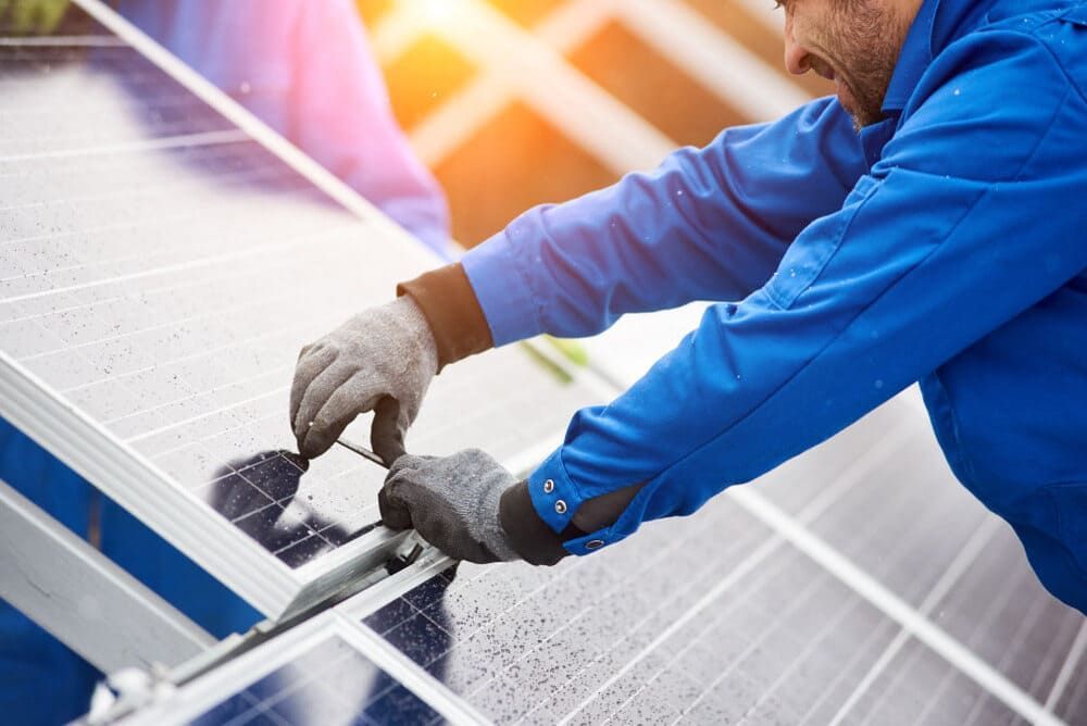 A Man In A Blue Jacket Is Working On A Solar Panel — Solarblu Pty Ltd In Tullimbar, NSW