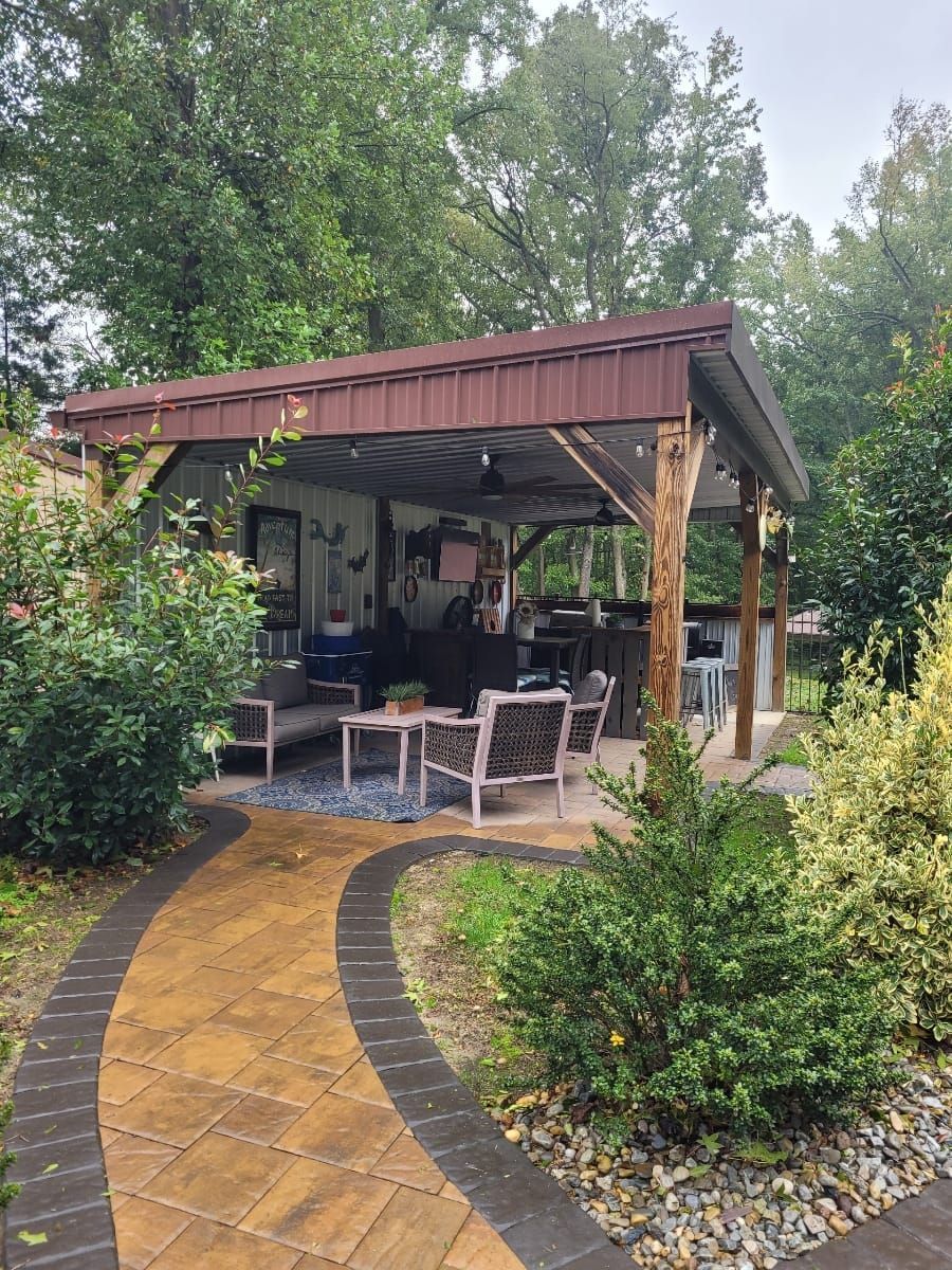 A covered outdoor patio with seating and bar area, accessed by a winding path, set amidst greenery.