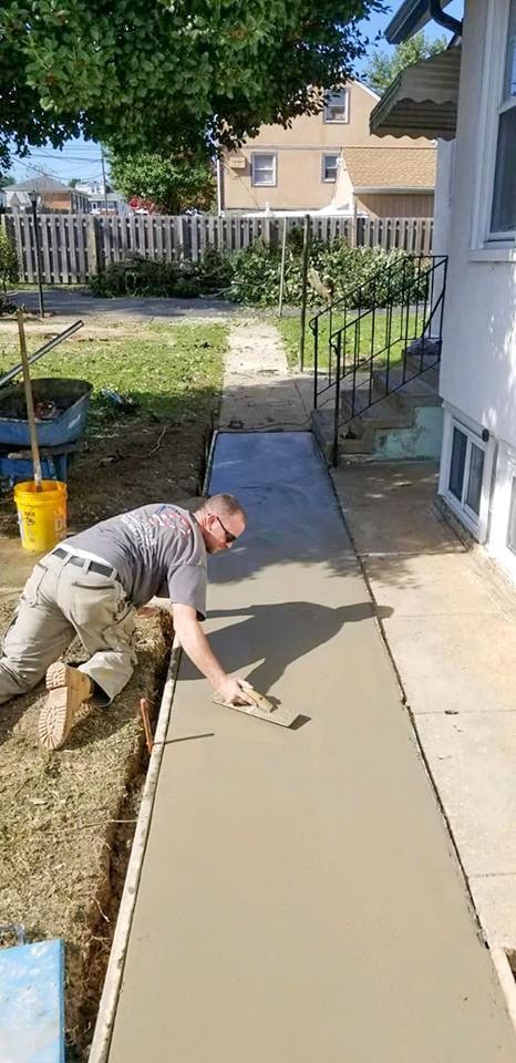 A man is laying concrete on a sidewalk in front of a house.