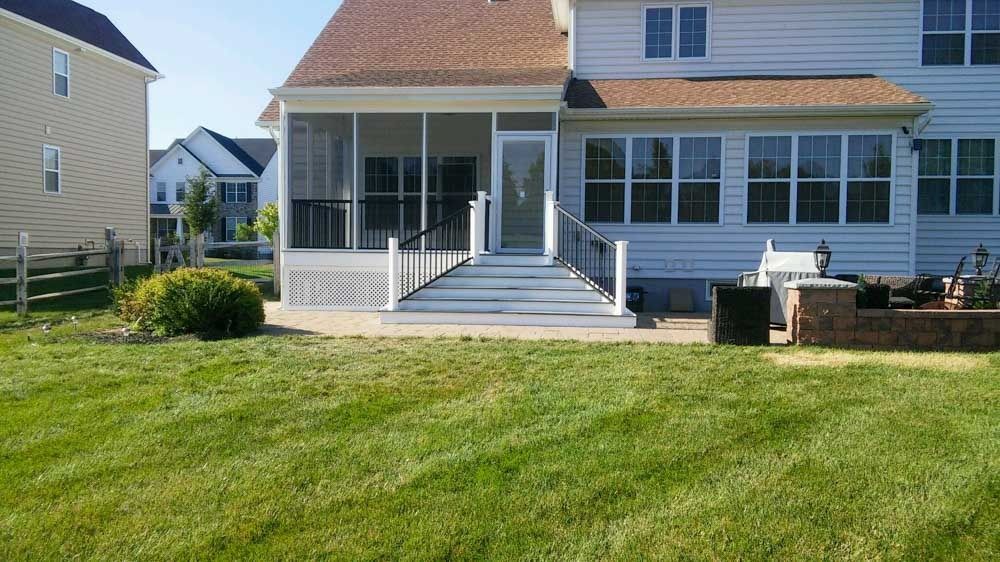 A white house with a screened in porch and a large lawn in front of it.