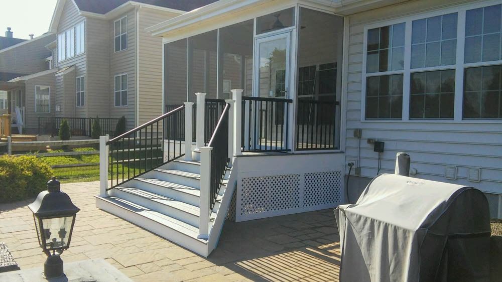 A screened in porch with stairs and a grill in front of a house.