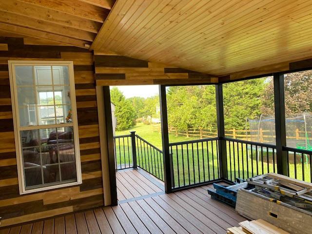 A screened in porch with wood paneling and a black railing