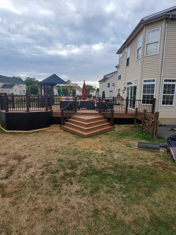 A large deck with stairs leading up to it is in the backyard of a house.