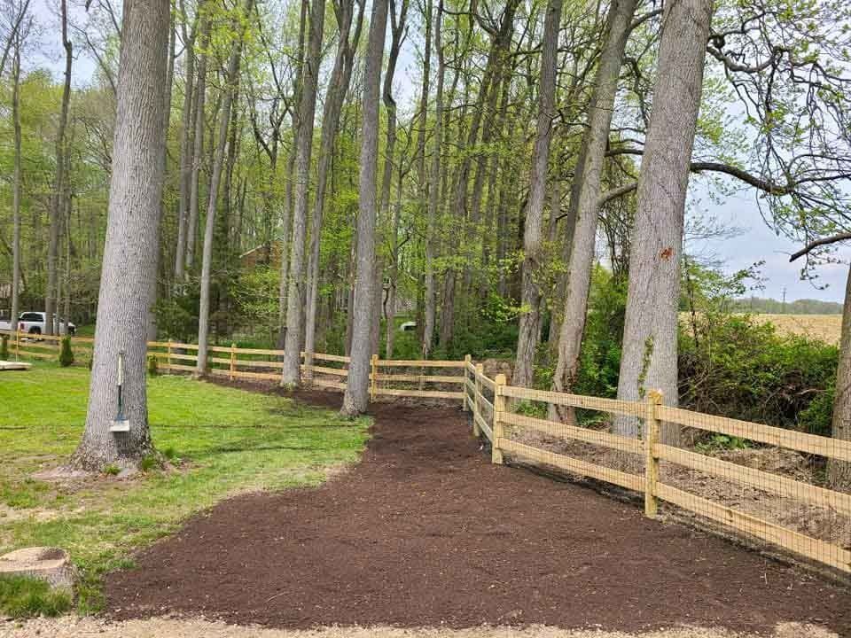 A wooden fence surrounds a dirt path in the middle of a forest.