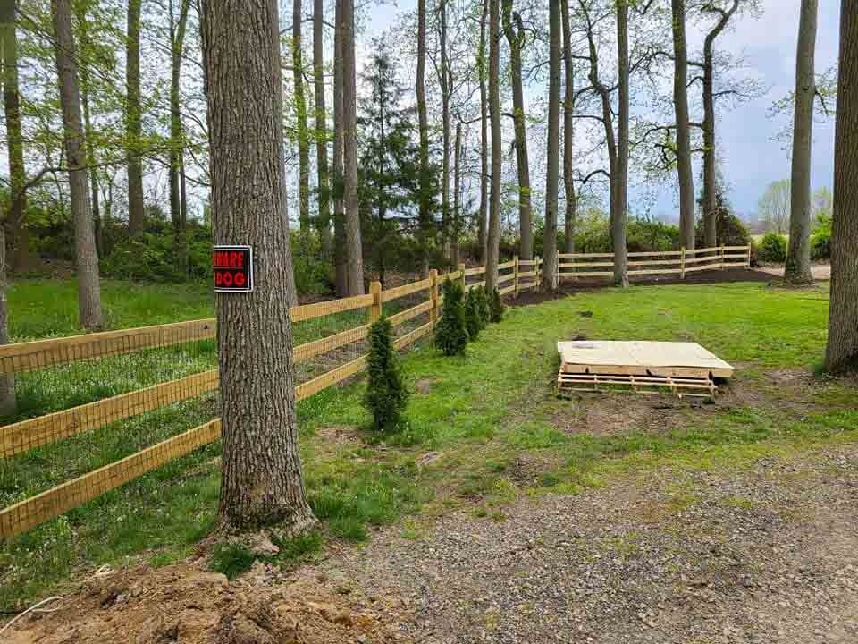 A wooden fence surrounds a grassy field in the middle of a forest.