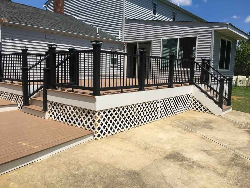 A deck with a black railing and stairs in front of a house.