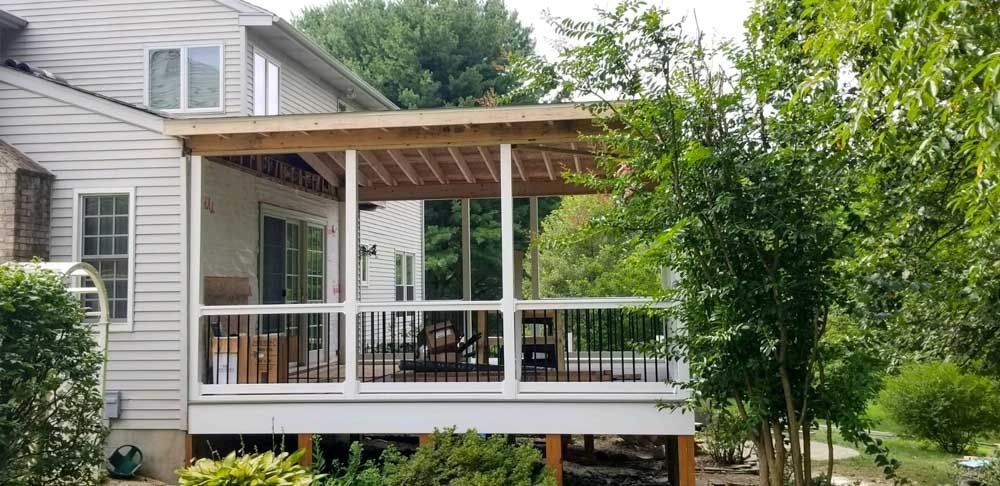 A white house with a large screened in porch surrounded by trees.