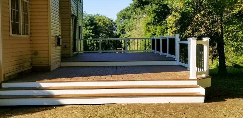 A large deck with stairs and a white railing is in front of a house.