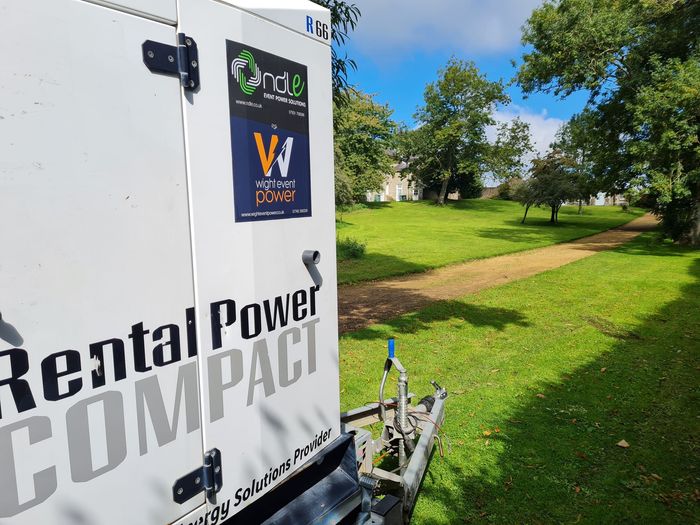 White Rental Power Compact trailer parked on grass in a sunny park with trees in the background