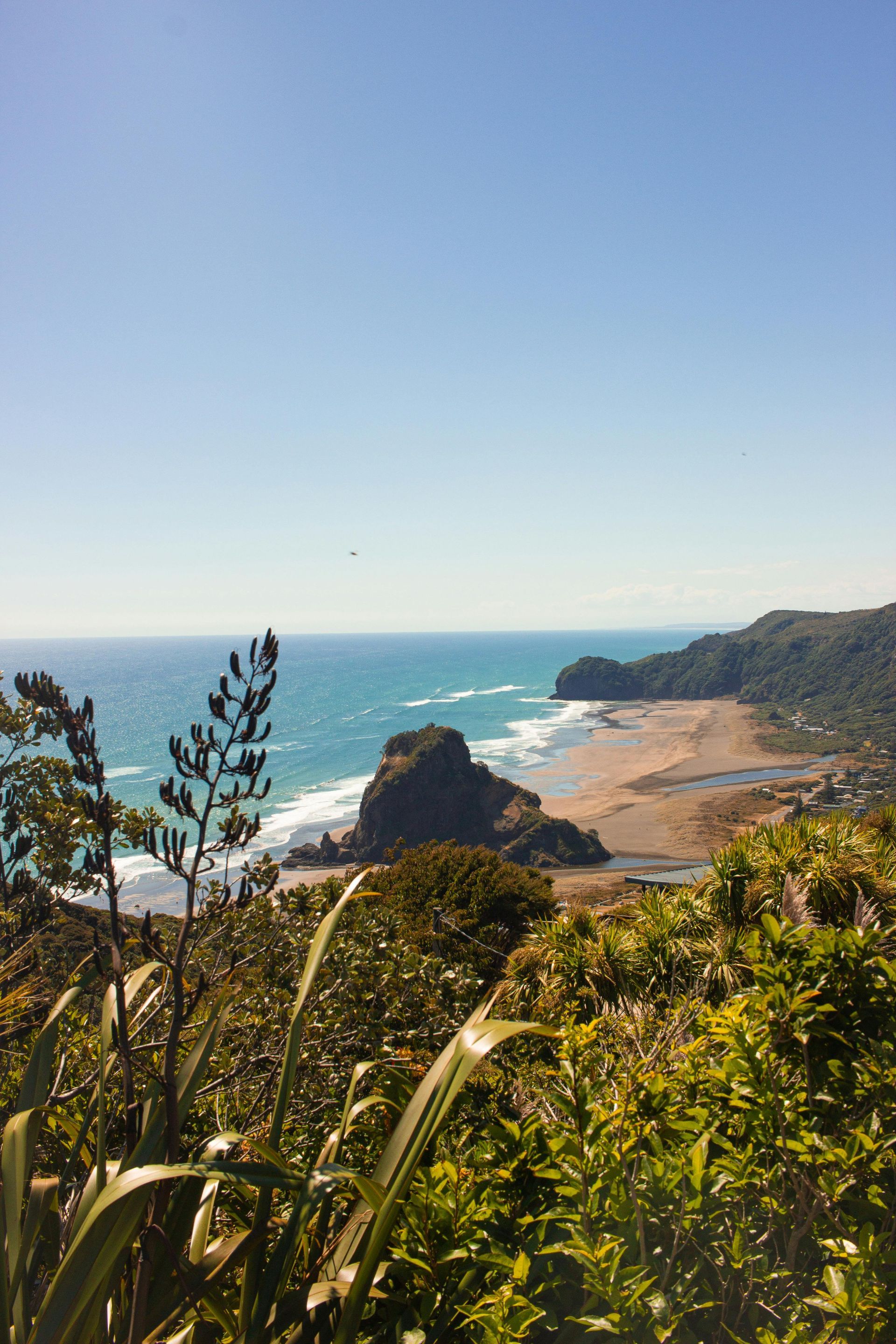 Ocean view of sandy beach and rocky headland under blue sky.