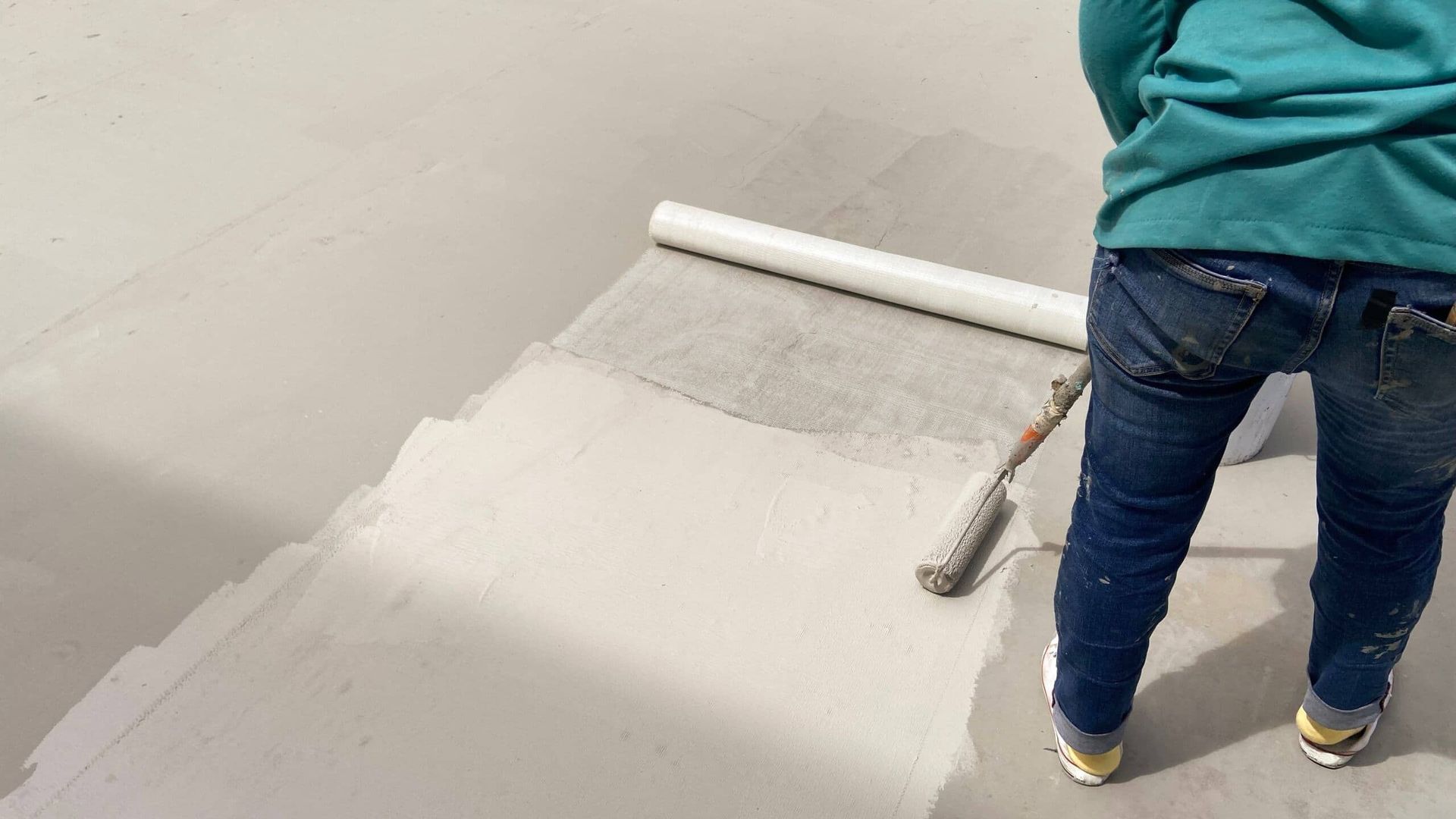 A Person is Painting a Concrete Floor With a Paint Roller — NHM Painting & Projects Pty Ltd in Ciccone, NT