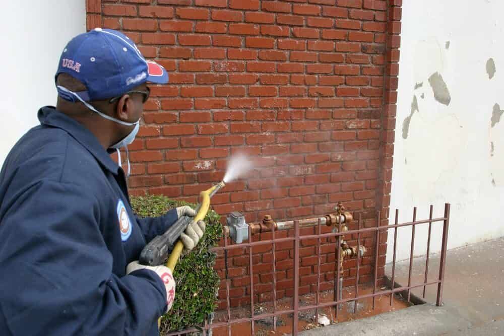 A Man Spraying a Brick Wall With a Hose — NHM Painting & Projects Pty Ltd in Ciccone, NT