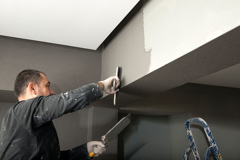 A Man is Painting a Wall With a Spatula — NHM Painting & Projects Pty Ltd in Ciccone, NT