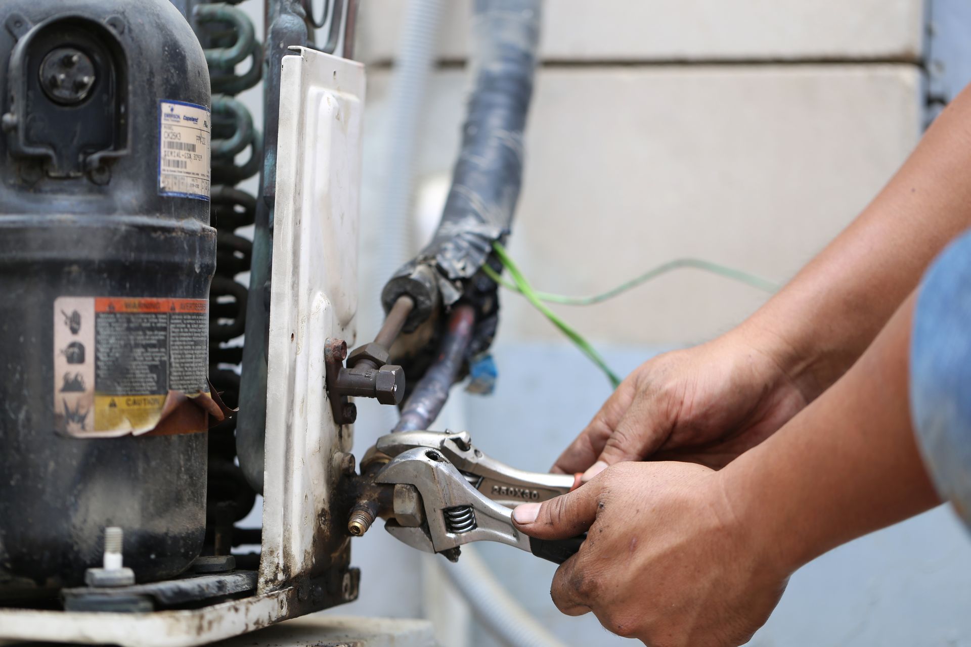 Hands use a wrench to tighten connections on HVAC equipment during indoor furnace maintenance.