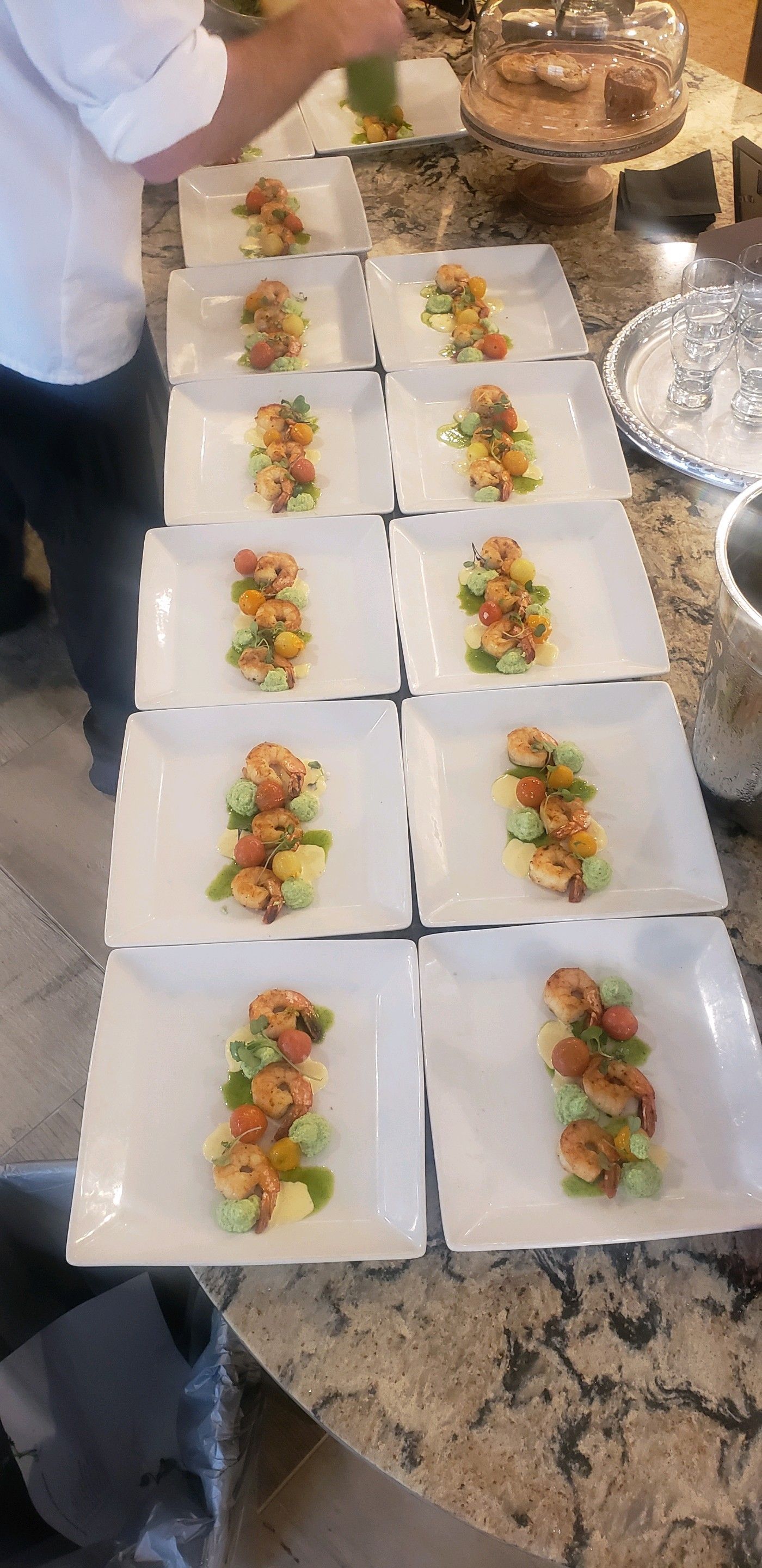 A chef plating appetizer courses on square white plates in a kitchen.