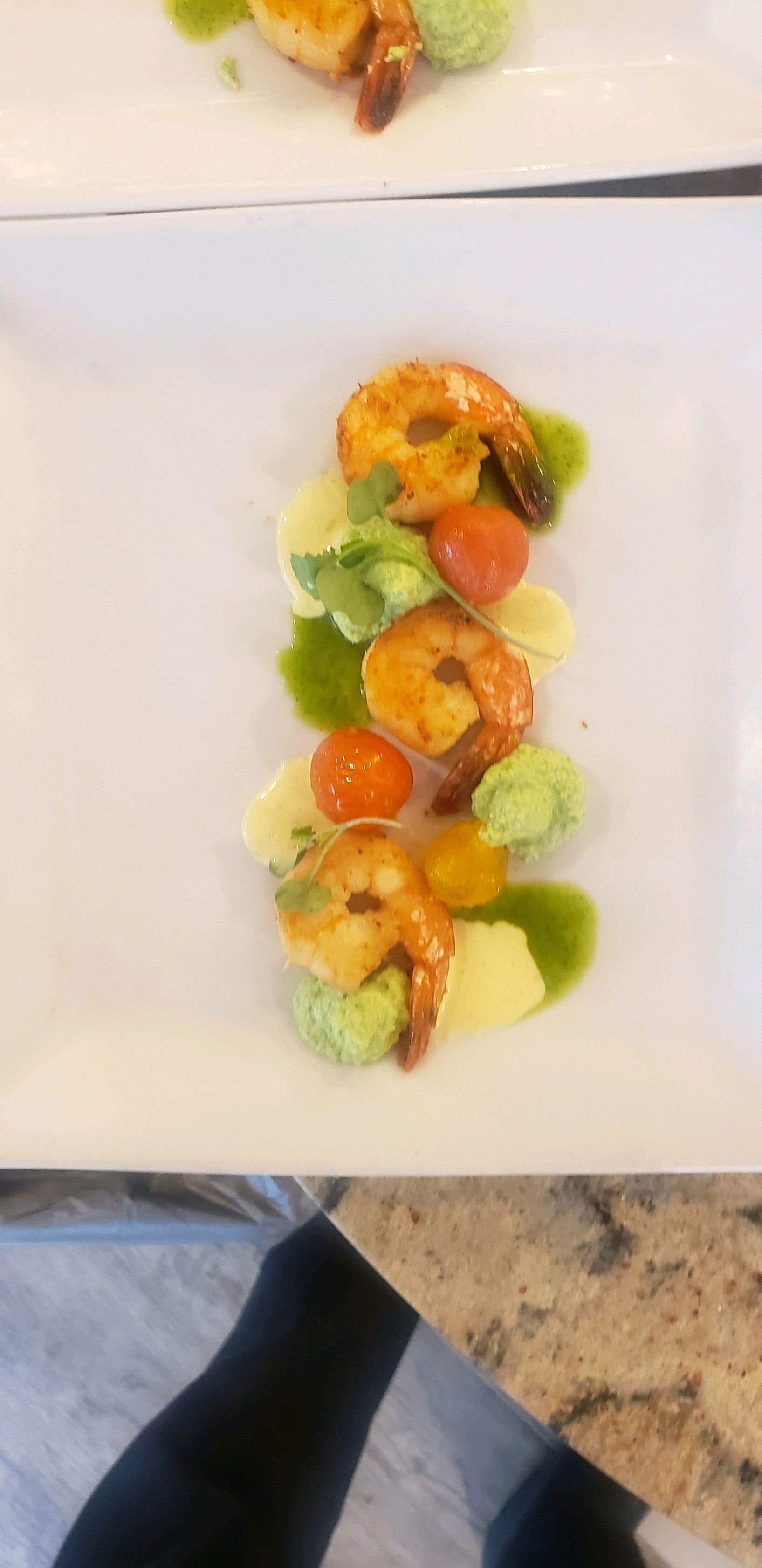 Shrimp dish on white plate with green sauce, tomatoes, and broccoli.