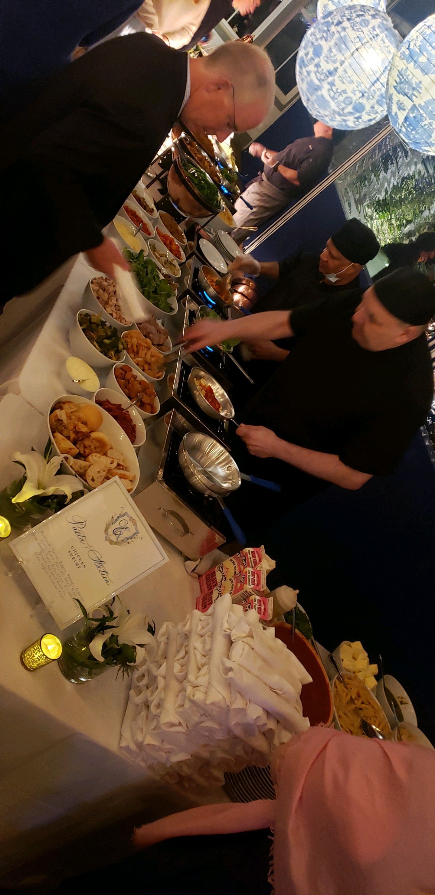 Buffet with food being served by staff, with guests. Lanterns and flowers decorate the tables.