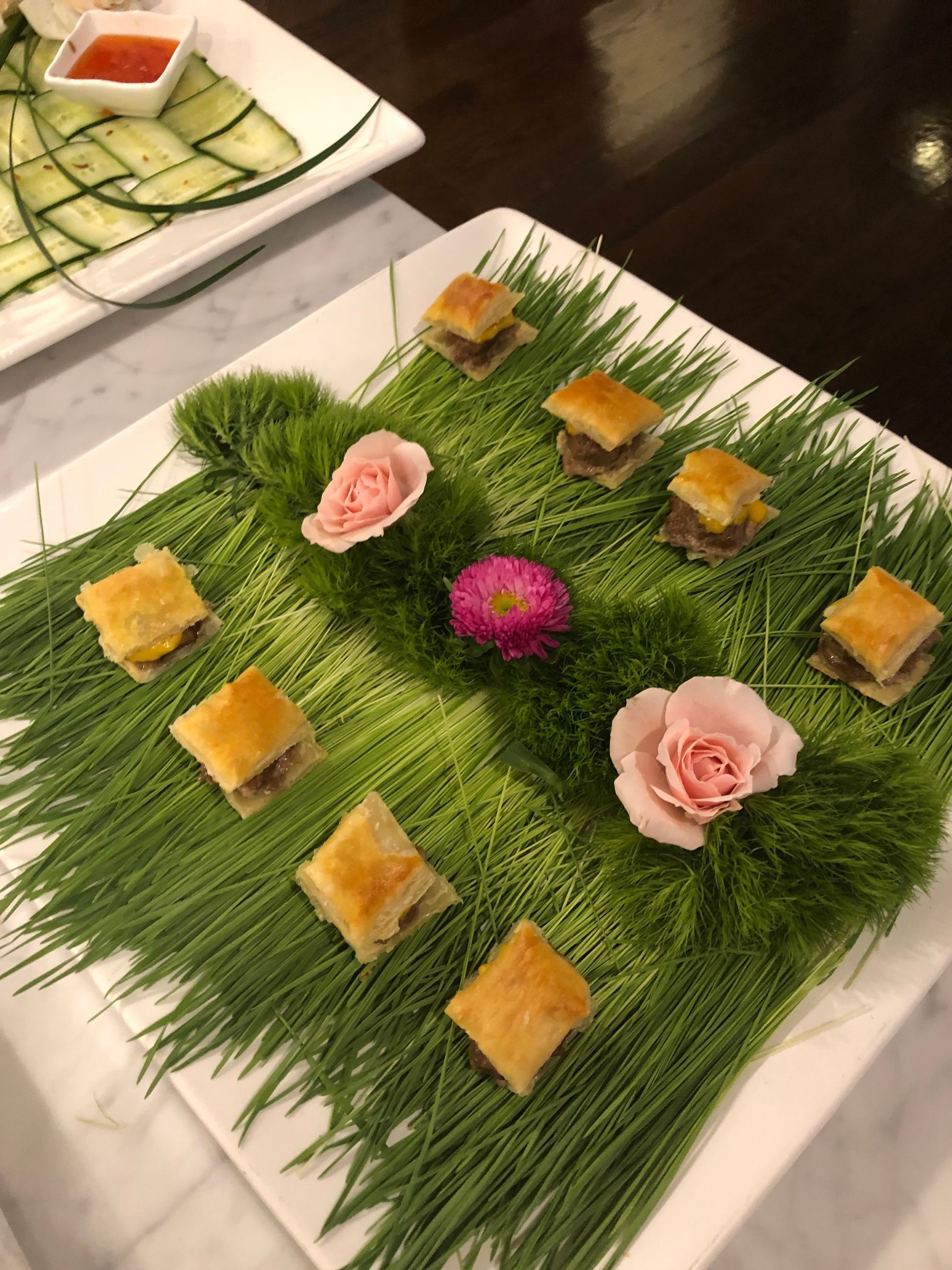 Square appetizers on green garnish with pink flowers, on a white plate.
