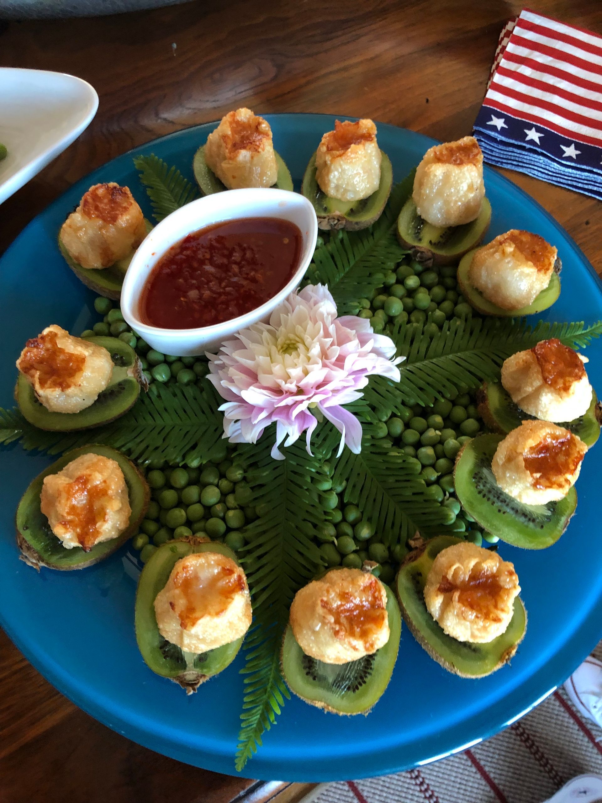 Appetizer: Seared scallops on kiwi slices arranged on a blue plate, with a dipping sauce and peas.