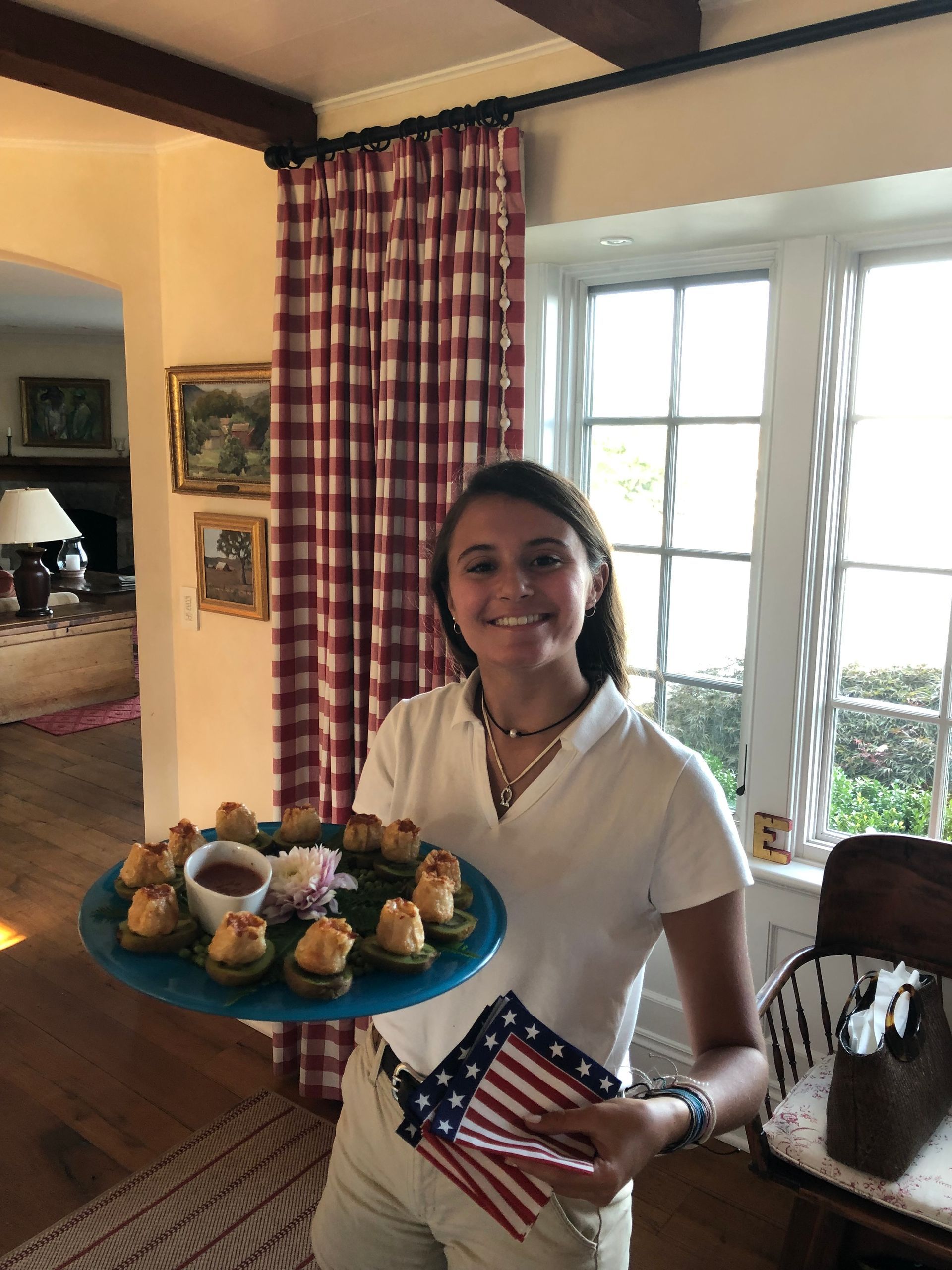 Teenage girl holding tray of appetizers and a small American flag indoors.