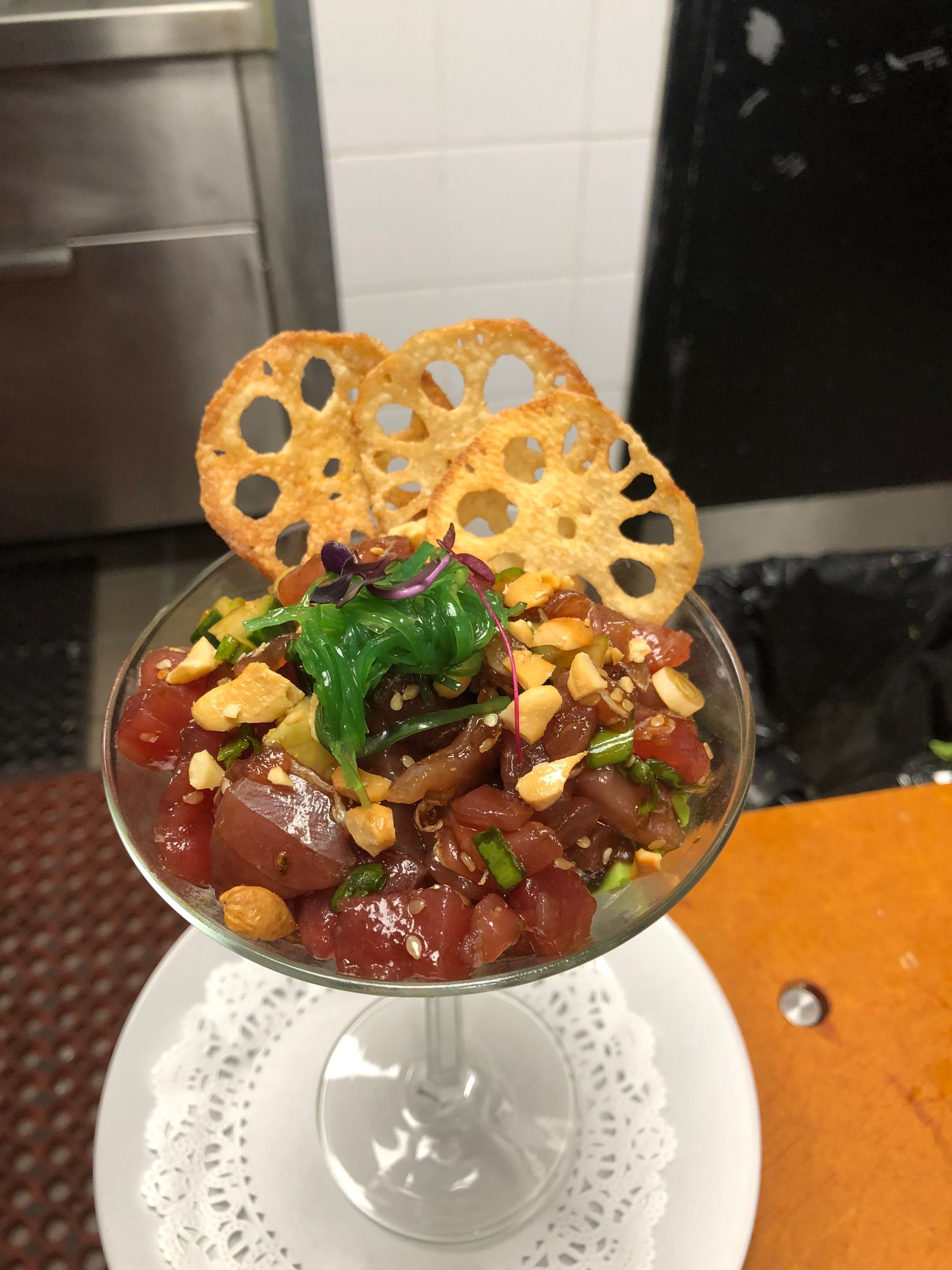 A tuna poke appetizer in a glass, garnished with lotus root chips and herbs.