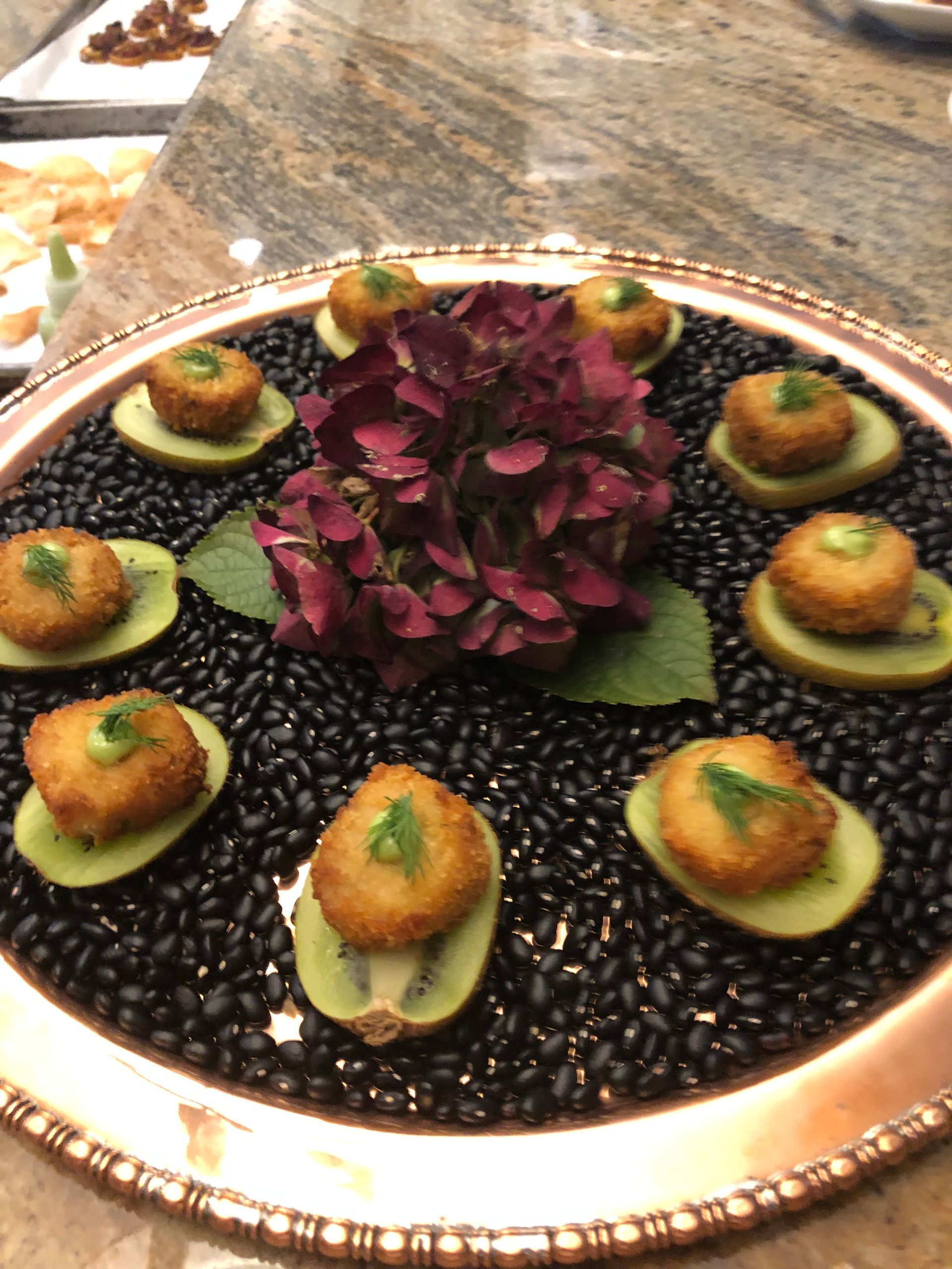 Appetizers on kiwi slices, black beans, around a flower.