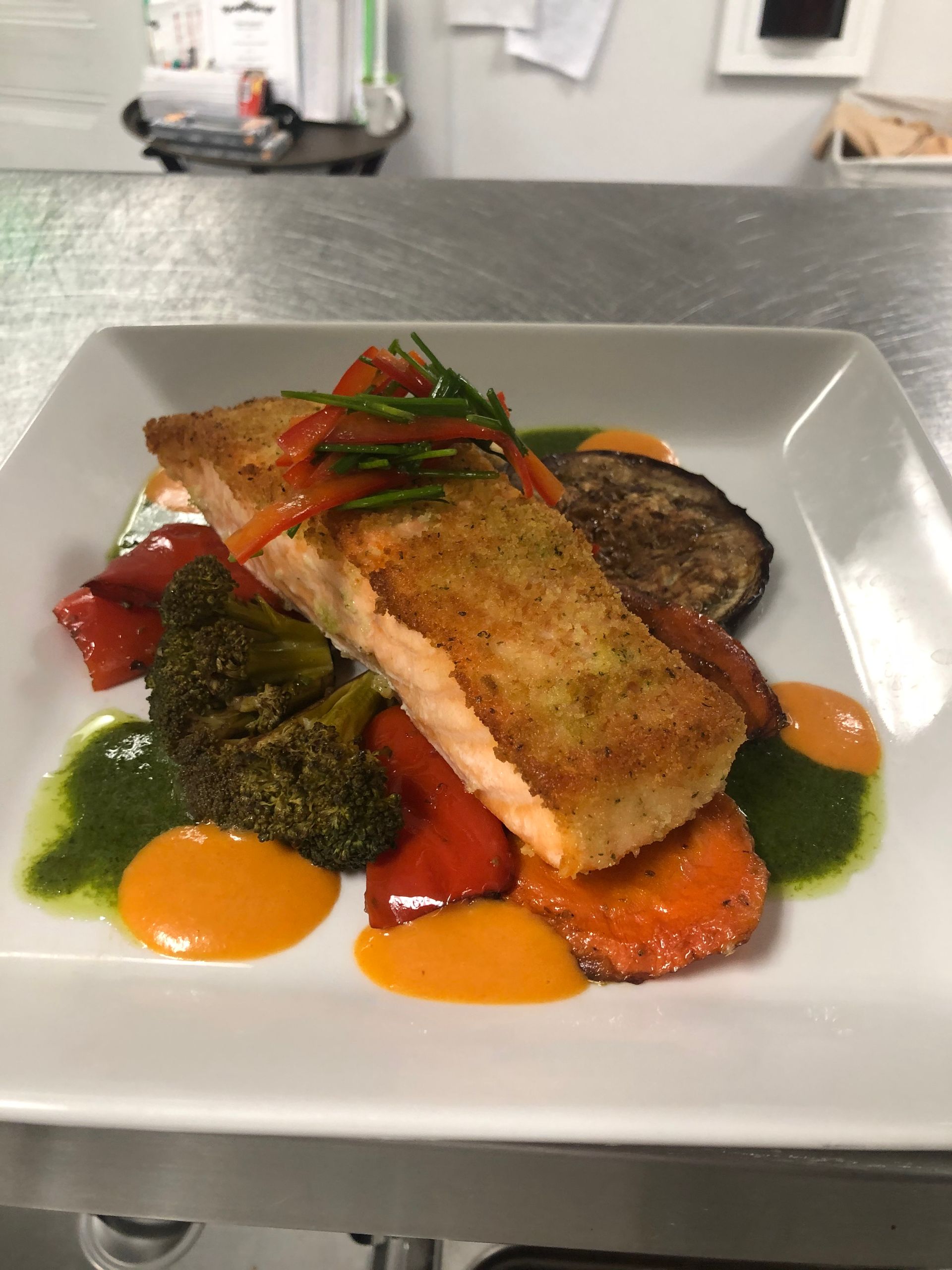 Salmon dish with roasted vegetables and sauces on a white plate.