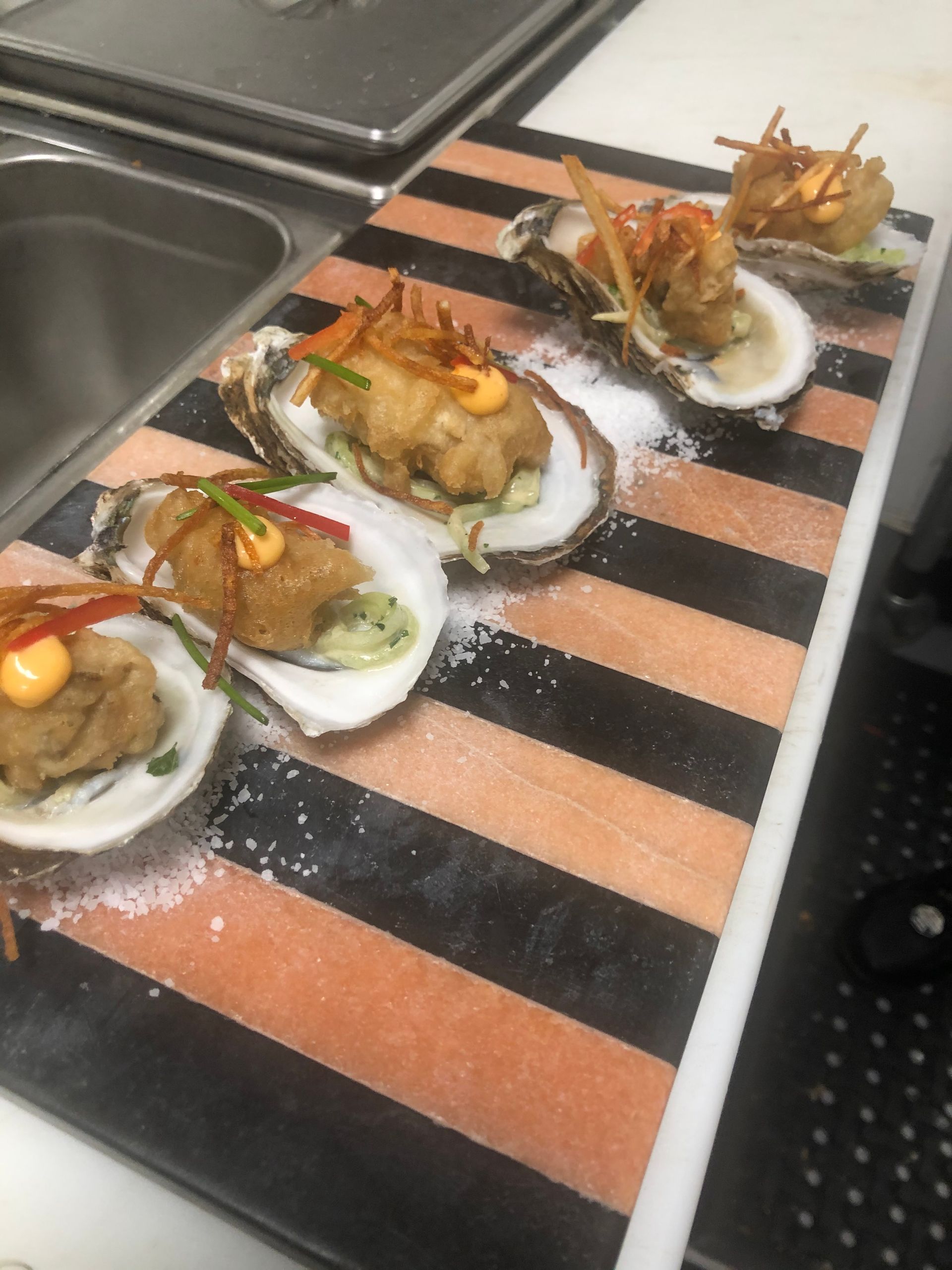 Fried oysters on the half shell, arranged on a black and orange striped wooden serving board with salt.