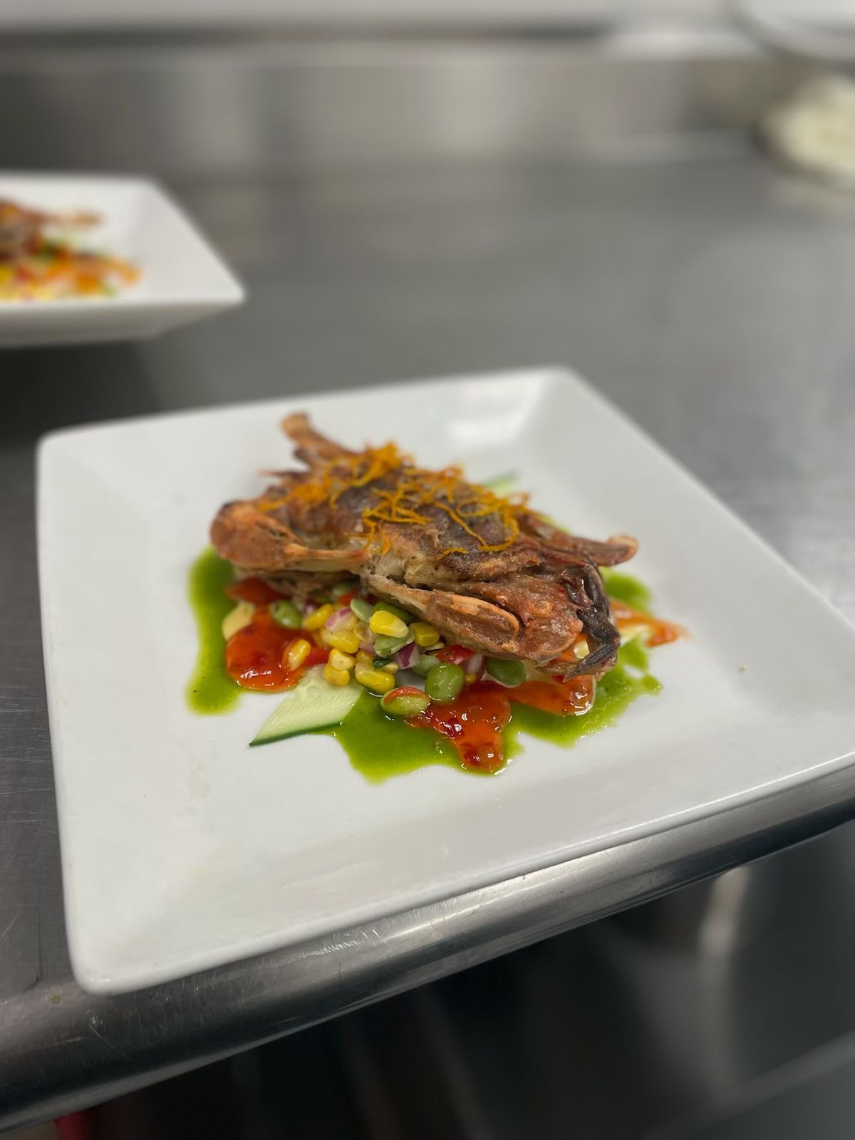 Crispy fried bird on a plate with colorful garnish and green sauce.