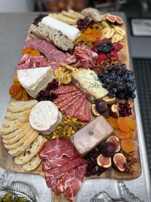 Charcuterie board: cheeses, meats, crackers, fruits, nuts on a wooden surface.