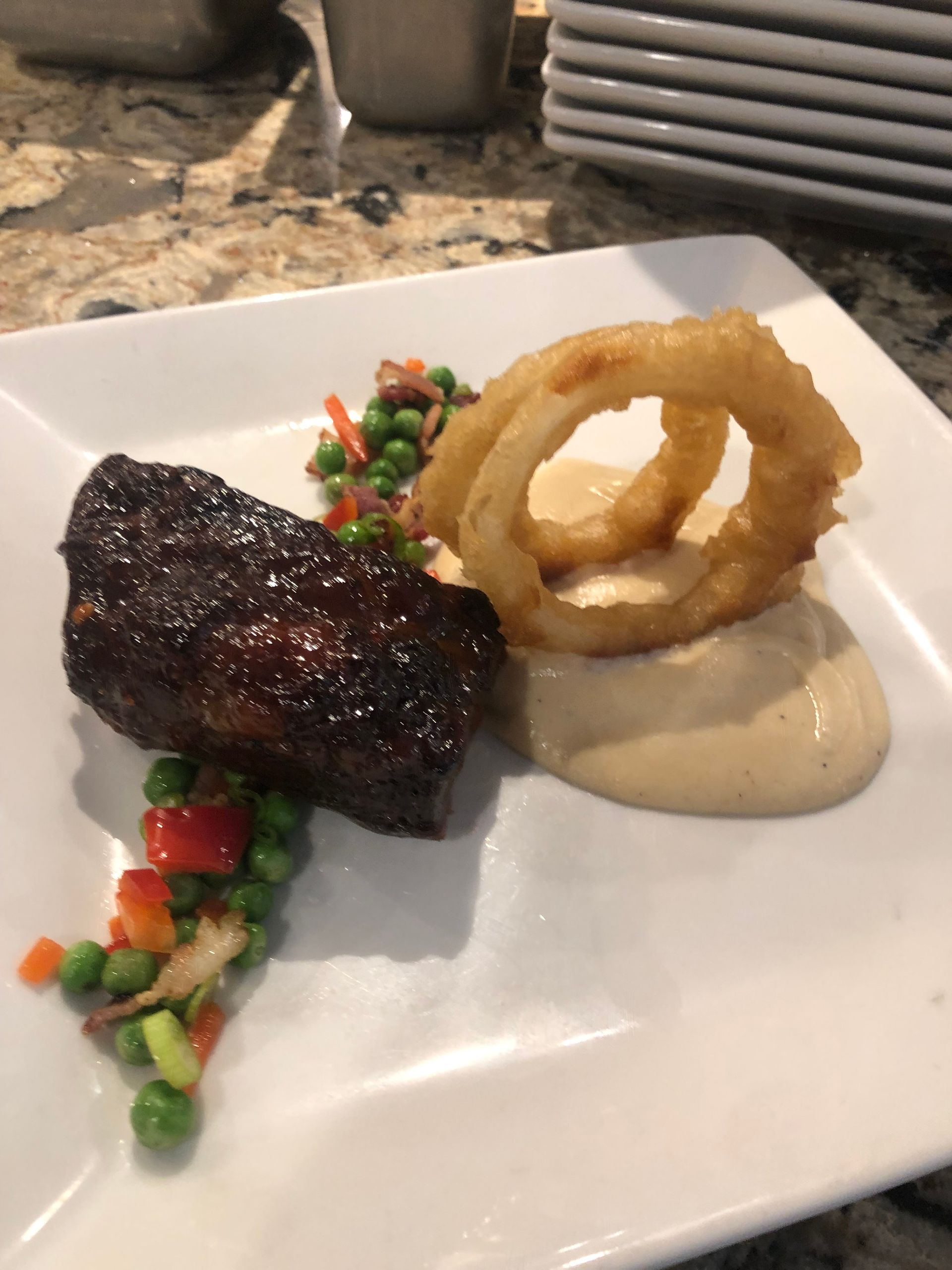 Plate of food: glazed meat, onion rings, sauce, and mixed vegetables.