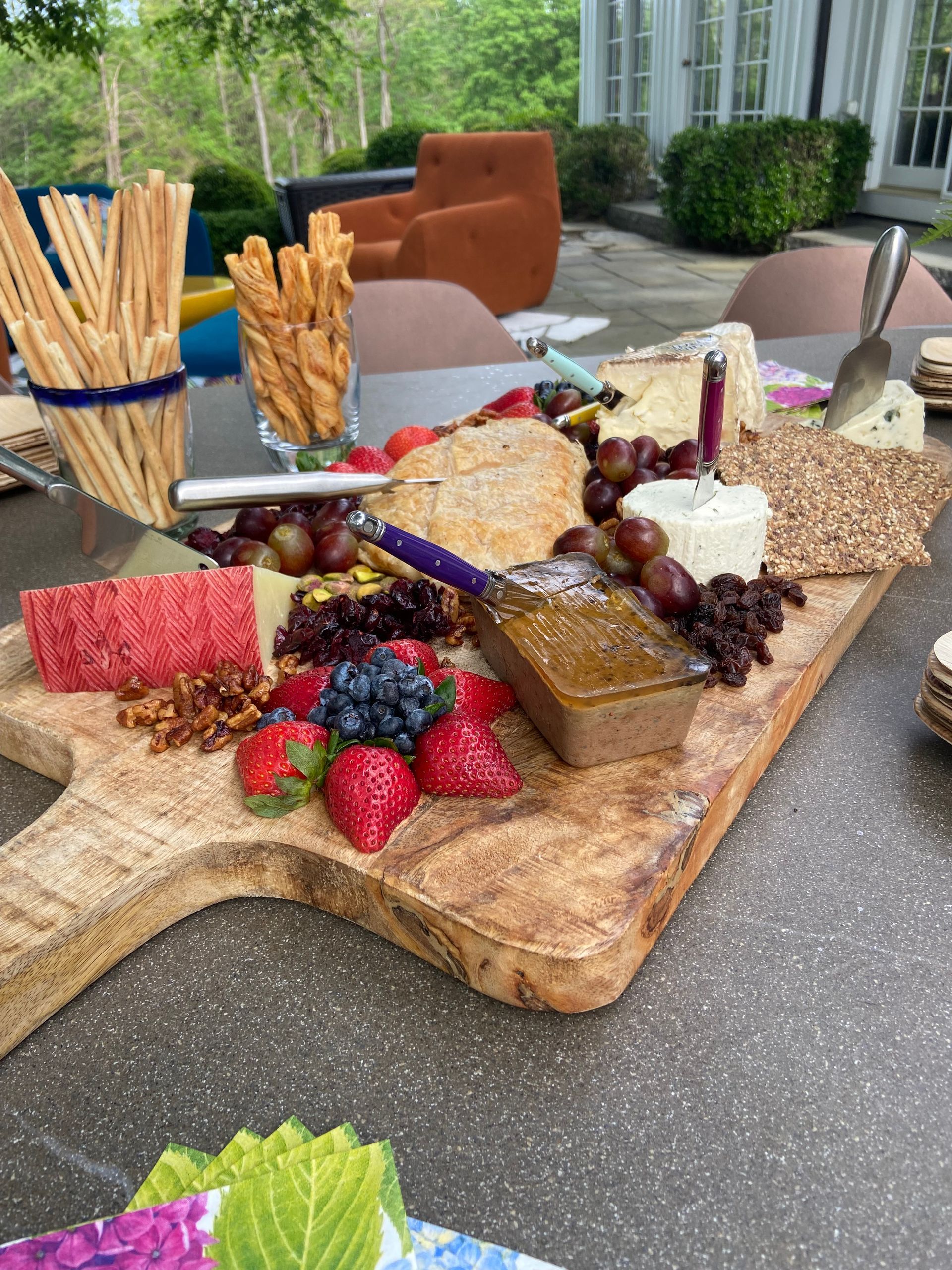 Woman placing food on a buffet table, others assisting. Indoor setting with curtains.