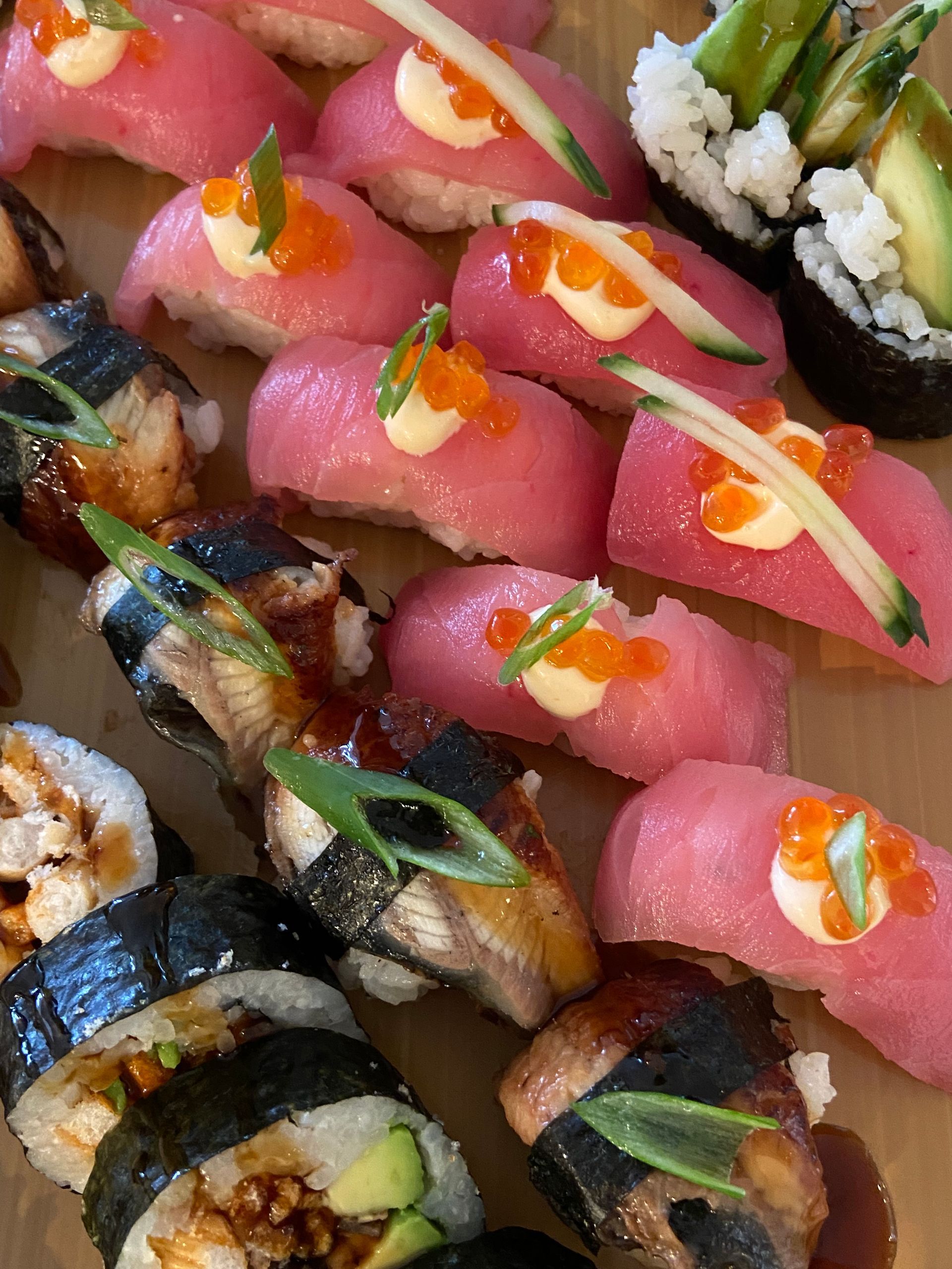 Sushi platter with various nigiri and rolls, featuring tuna, eel, avocado, and roe.