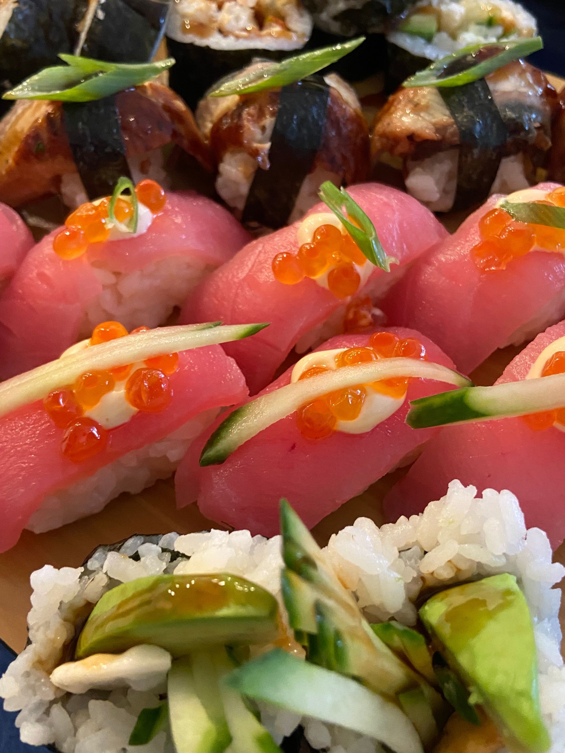 Sushi platter, featuring nigiri with salmon roe, and maki rolls with avocado and cucumber.