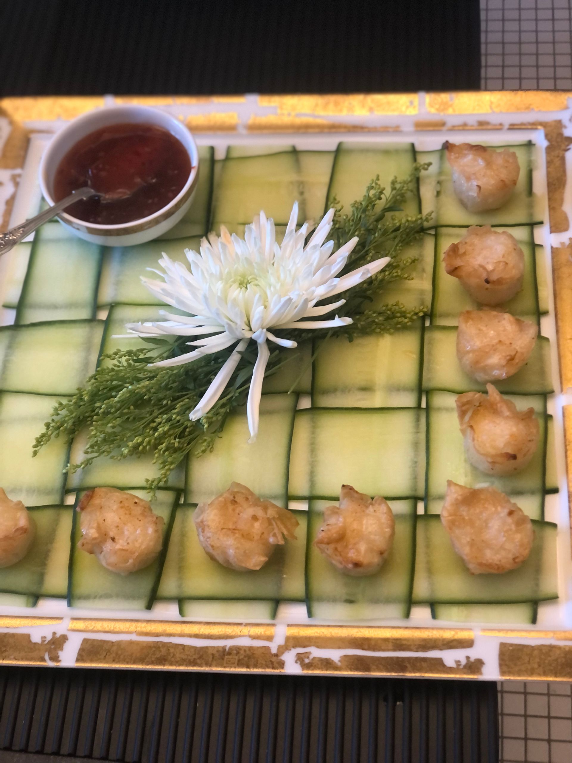 Appetizer platter with fried food, sauce, flower, and cucumber grid.