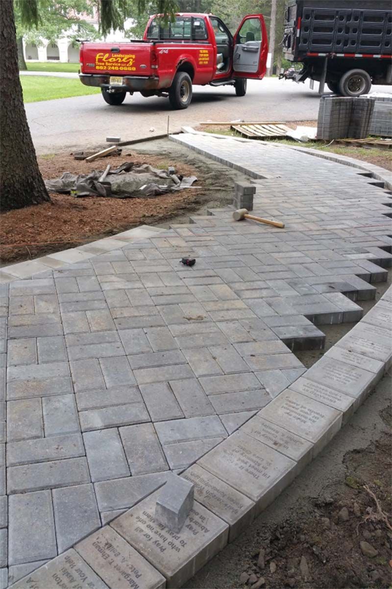 Sidewalk construction: gray pavers being laid, red truck in background.
