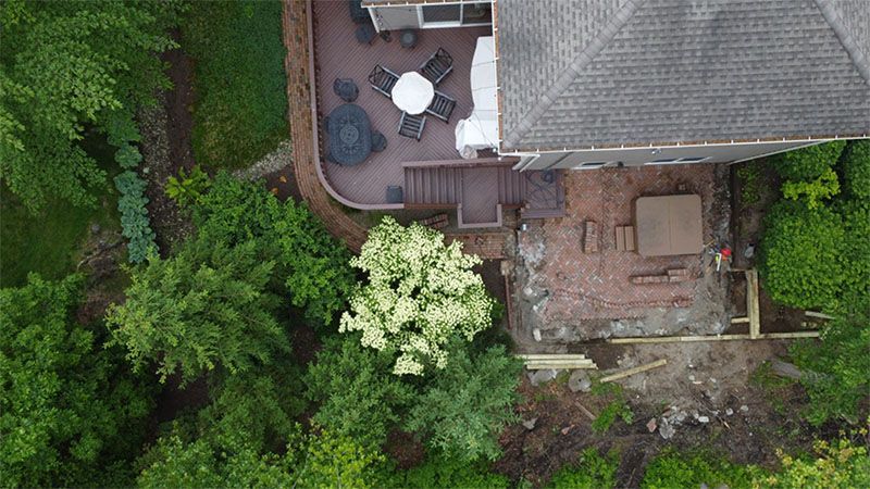 Overhead view of a house with a deck, a brick patio under construction, and lush green landscaping.