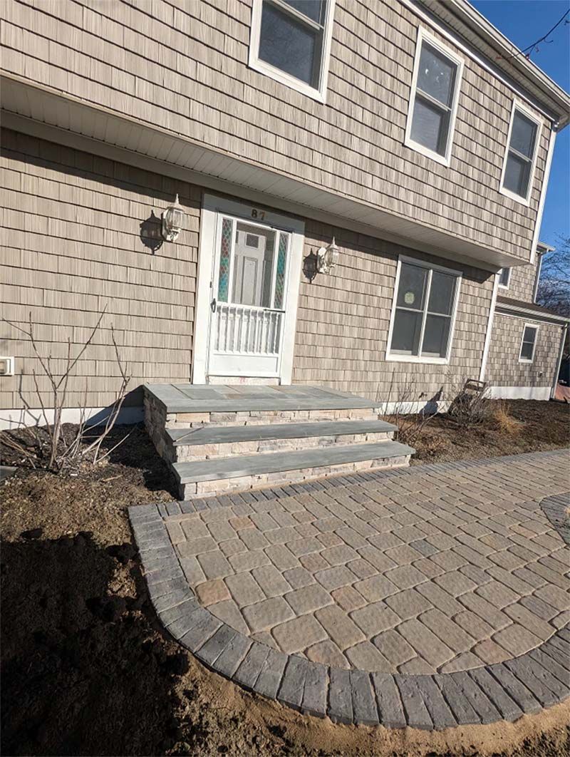 Exterior of a two-story house with steps leading to the front door, and a brick patio in front.